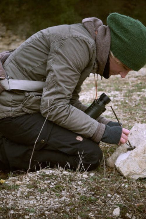 Wildnispädagogin Miriam kniet am Boden und untersucht ein Eulennest
